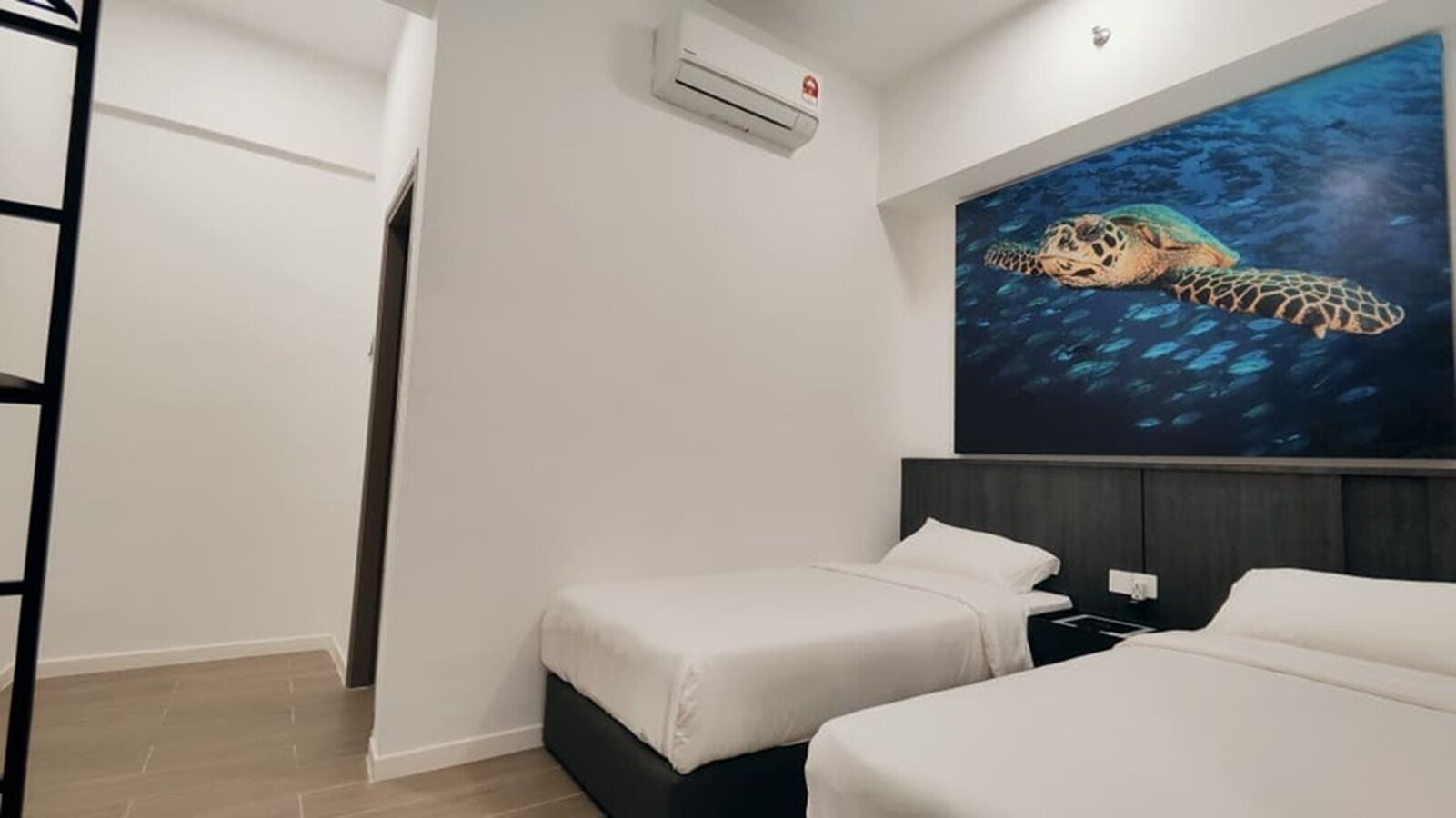 A hotel room with two beds, a painting of a sea turtle, and an air conditioning unit.