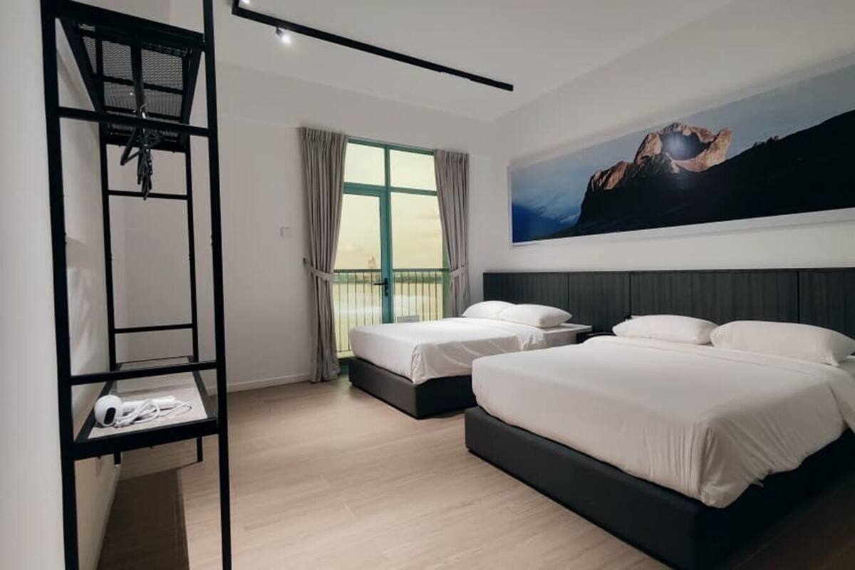 A modern hotel room with two beds, a large window with curtains, a black metal shelf with a white item, and a mountain landscape painting on the wall.