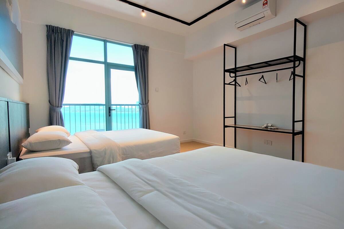 A hotel room with two beds, a window with curtains, a built-in wardrobe, and an air conditioning unit.