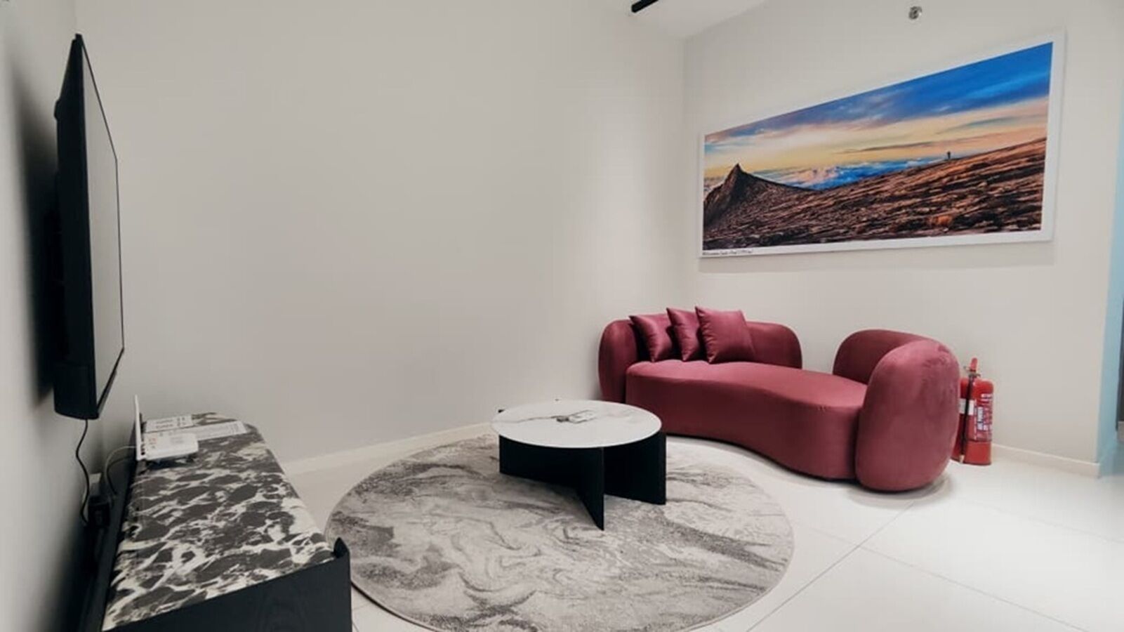 A modern living room with a flat-screen TV, a marble-patterned coffee table, a red sofa, and a large landscape painting on the wall.