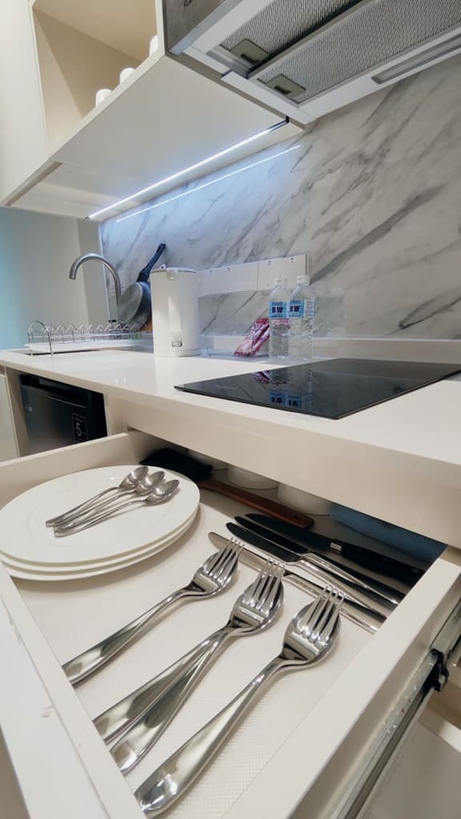Una cucina moderna con piano cottura integrato, mobili bianchi e una parete di fondo in marmo.