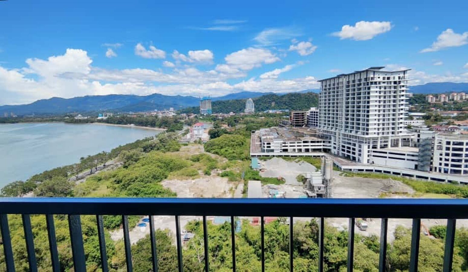 A coastal cityscape with a large hotel featuring multiple floors and a modern design, situated near a body of water and green areas.