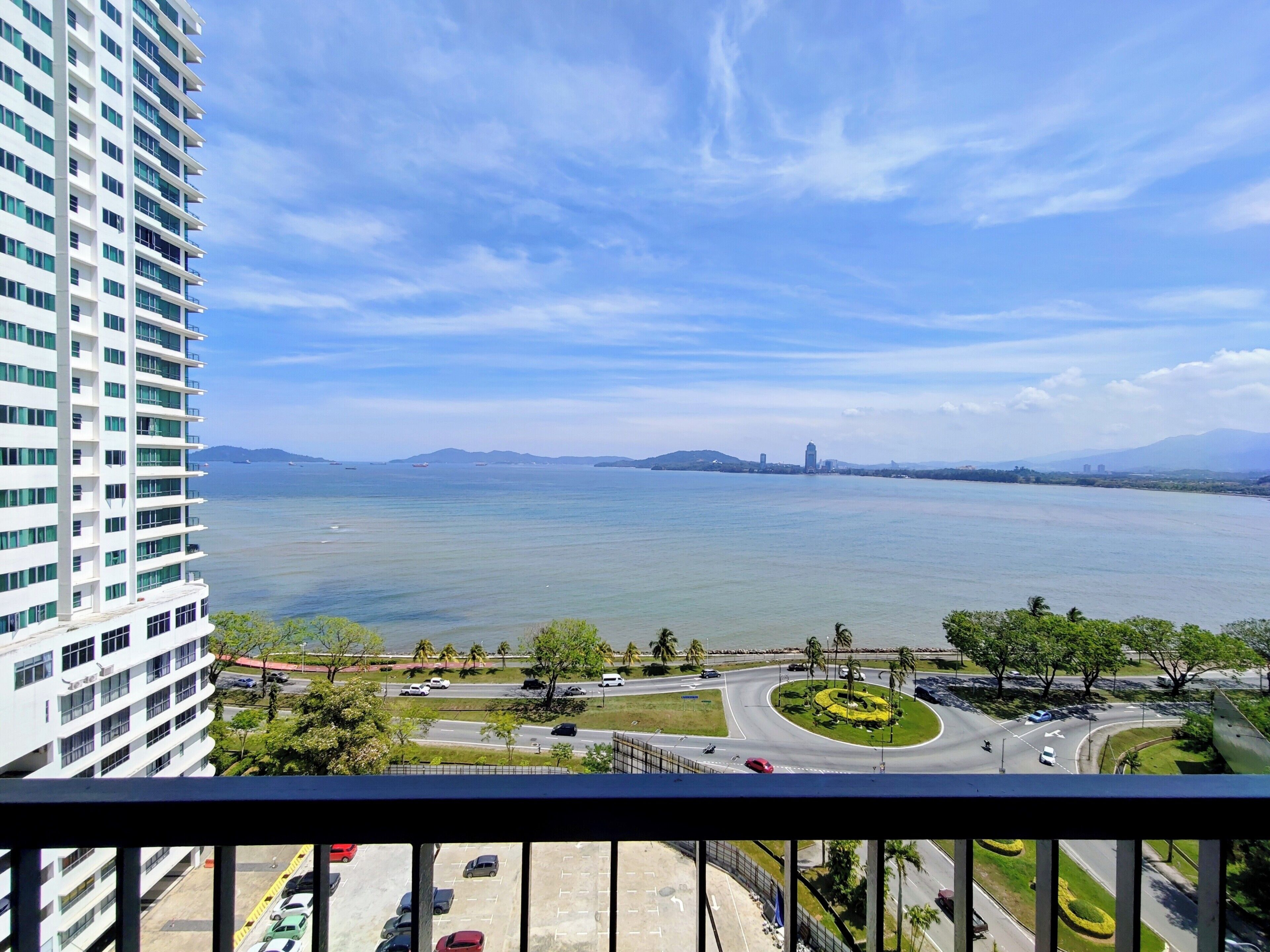 A high-rise building with a view of a large body of water, a roundabout, and distant mountains.