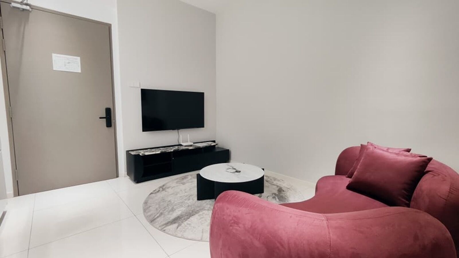 A modern living room with a flat-screen TV mounted on the wall, a round coffee table, and a pink sofa.