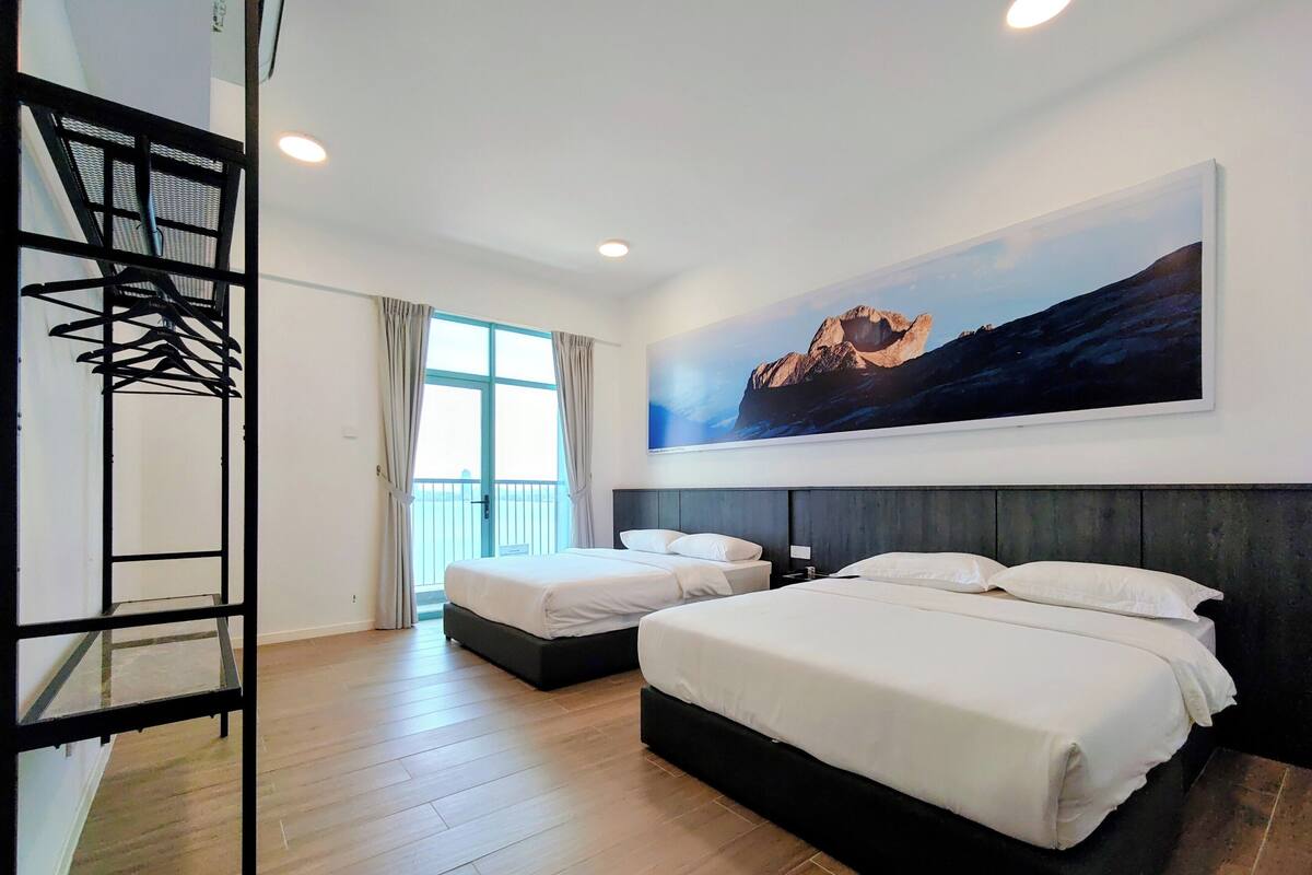 A hotel room with two beds, a large window with curtains, a metal rack, and a painting on the wall.