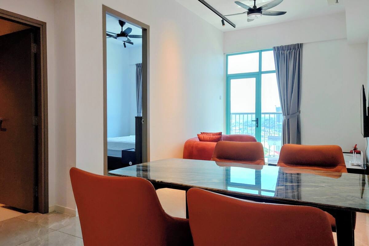 A modern hotel room with a large window, a ceiling fan, a dining table with chairs, and a bed with a view.