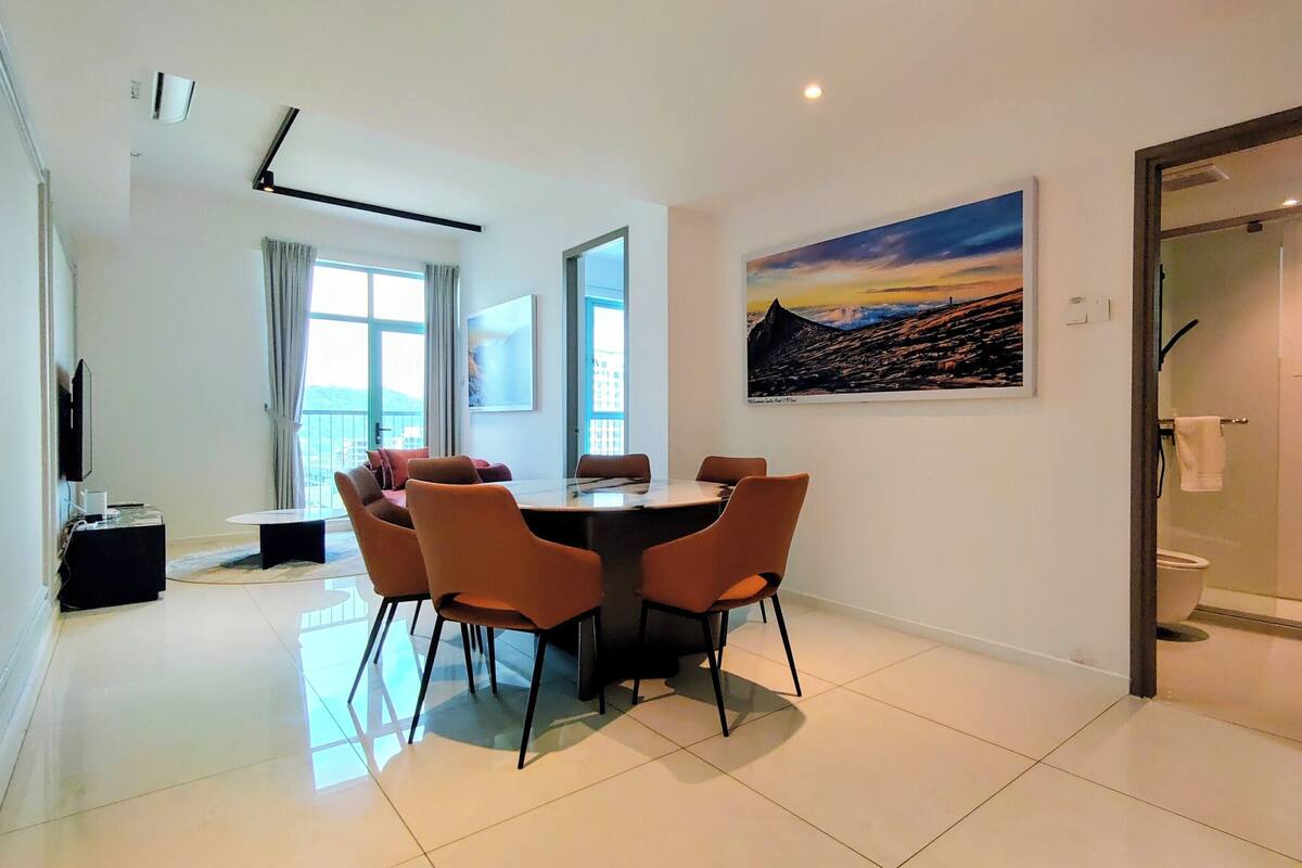 A modern dining area with a round table and orange chairs, a painting on the wall, and a view through the window.