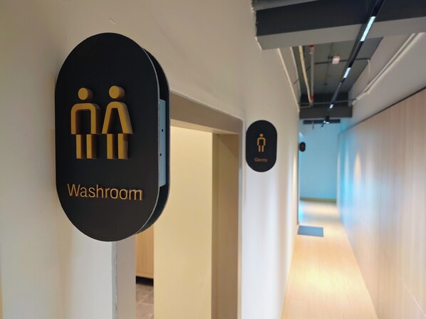 En hall med en svart skylt som visar var toaletten finns, och en separat skylt för herrtoaletten.