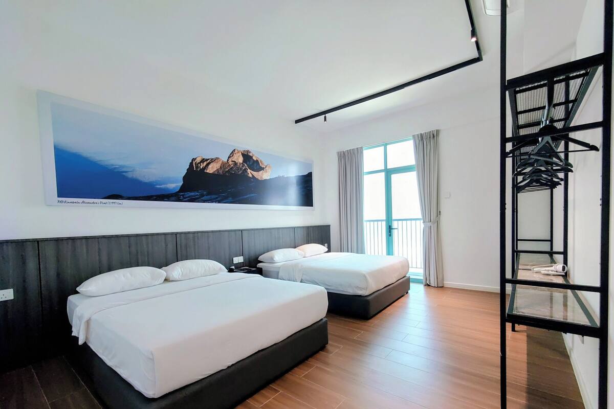 A hotel room with two beds, a large window, a balcony, and a wall-mounted TV.