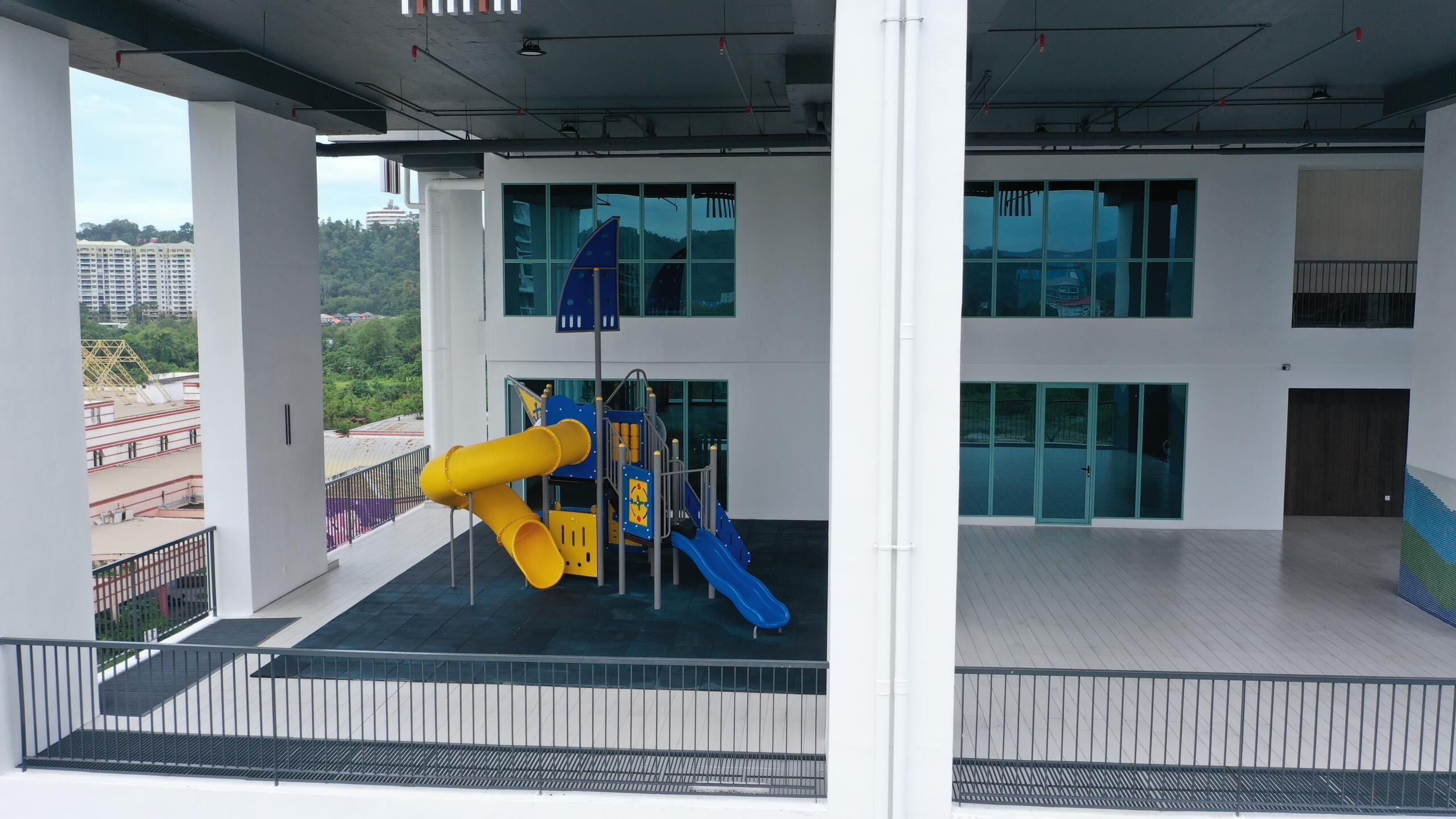 A modern building with a playground featuring yellow and blue slides, large windows, and a view of surrounding buildings.