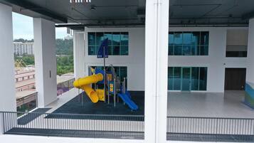 A modern building with a playground featuring yellow and blue slides, large windows, and a view of surrounding buildings.