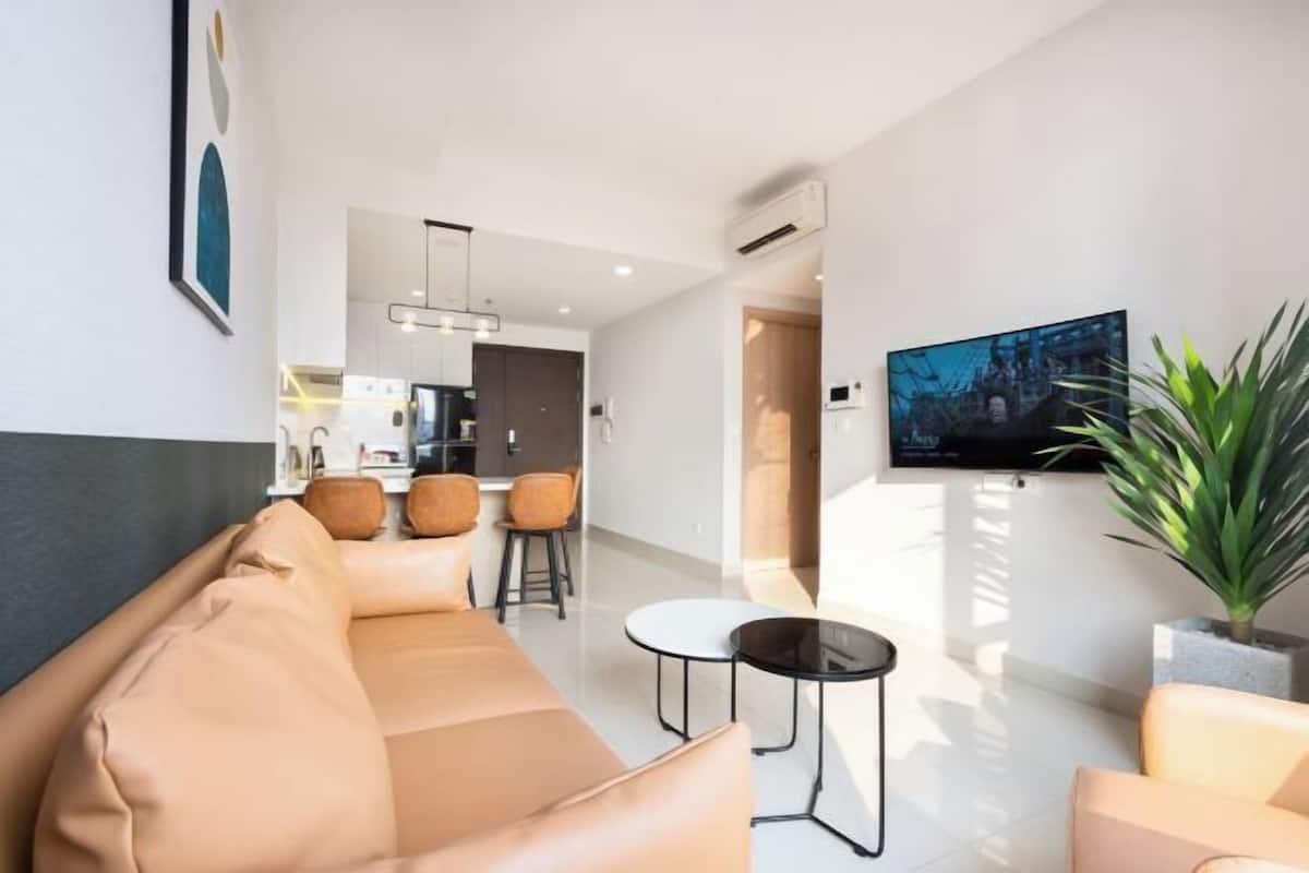 Ein modernes Wohnzimmer mit einer Couch, Sesseln, einem Couchtisch, einem Fernseher und einer Topfpflanze.