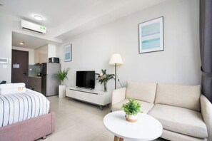 A modern hotel room with a bed, a sofa, a TV, a small table with a plant, and a kitchen area in the background. - MIN' Apartment - Rivergate Residence Downtown BUI VIEN - FREE POOL (Ho Chi Minh City)