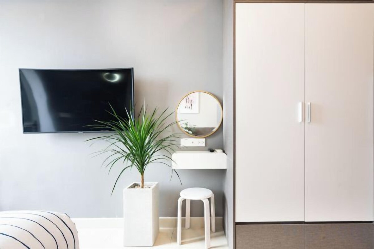A modern room with a flat-screen TV mounted on the wall, a potted plant, a small stool, and a wardrobe.