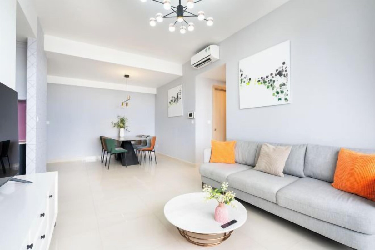 A modern living room with a grey sofa, a round coffee table, and a dining area with chairs and a table.