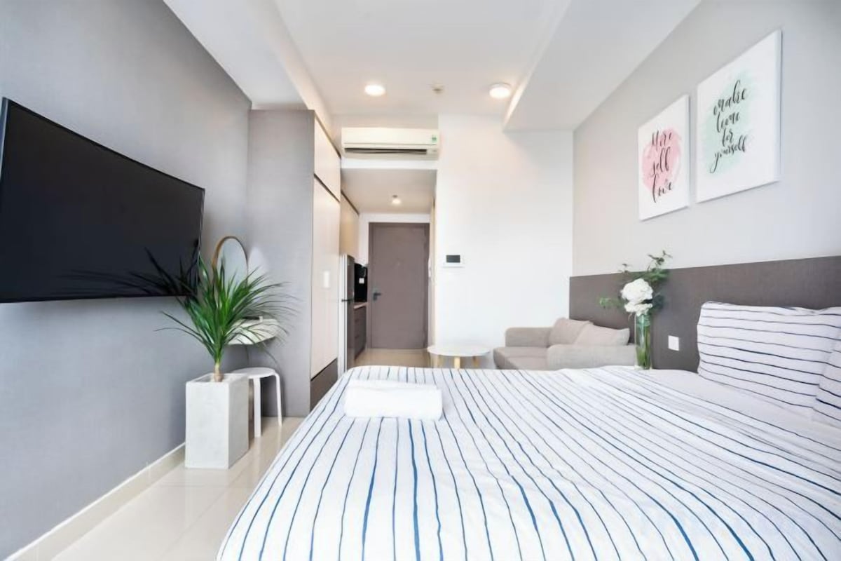 Une chambre à coucher moderne avec un grand lit, un téléviseur à écran plat, une plante en pot et une petite table.