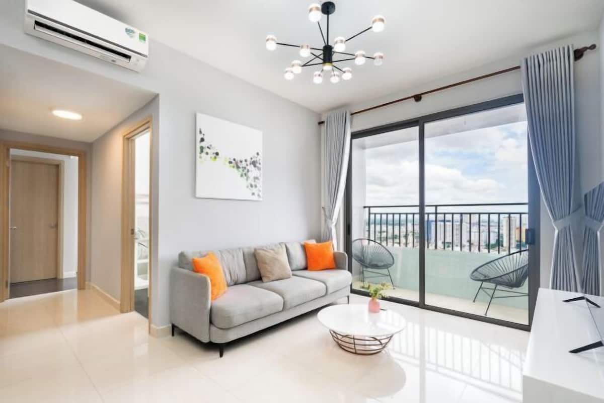Ein modernes Wohnzimmer mit einem grauen Sofa, einem runden Couchtisch und einer großen Schiebeglastür, die auf einen Balkon führt.
