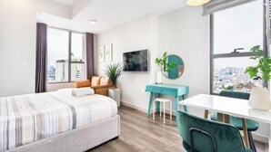 A modern hotel room with a large bed, a desk, a chair, a TV, and a window with a city view. - MIN' Apartment - Rivergate Residence Downtown BUI VIEN - FREE POOL (Ho Chi Minh City)