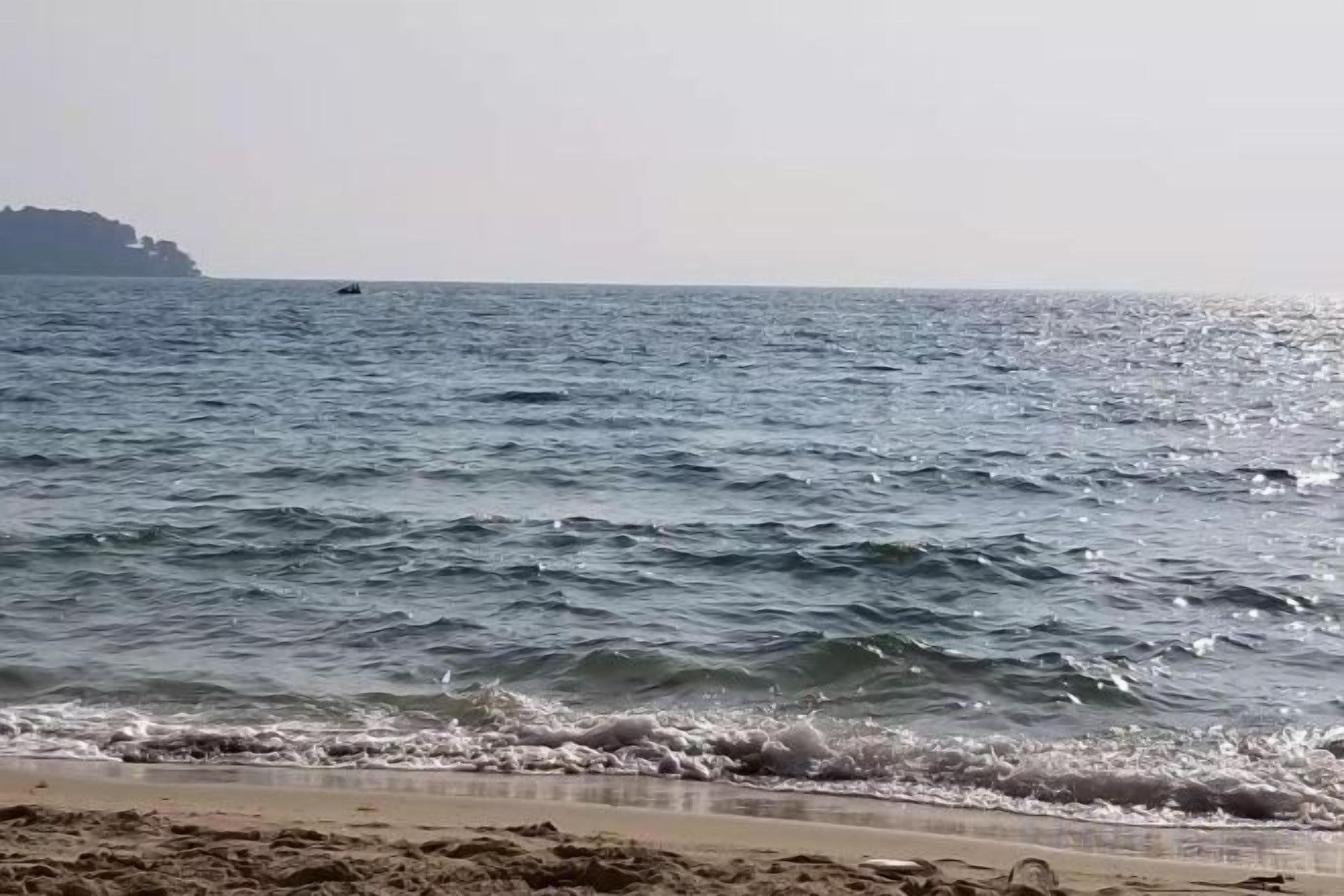 Une plage avec des vagues et une étendue de terre visible au loin.