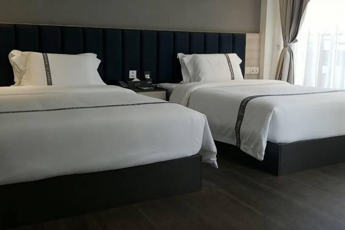 A hotel room with two beds, a dark headboard, a nightstand, and a window with curtains.