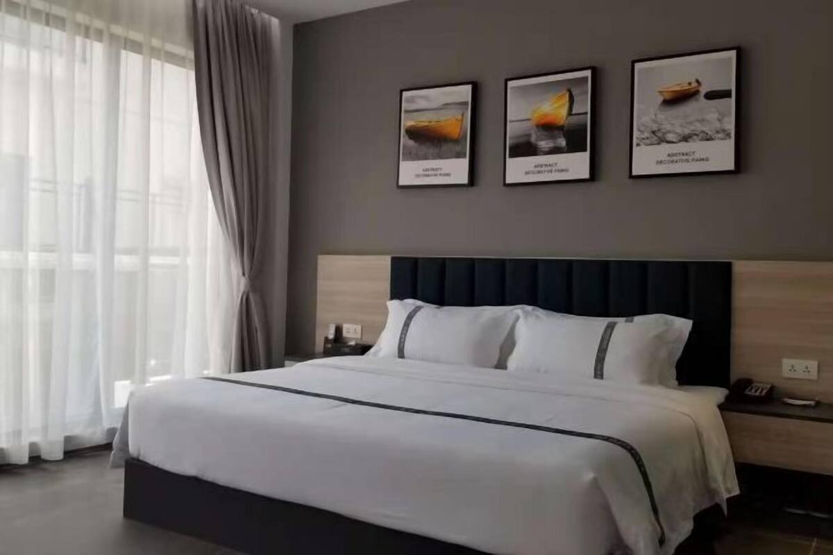 A modern hotel room with a large bed, a dark headboard, and three framed pictures on the wall.