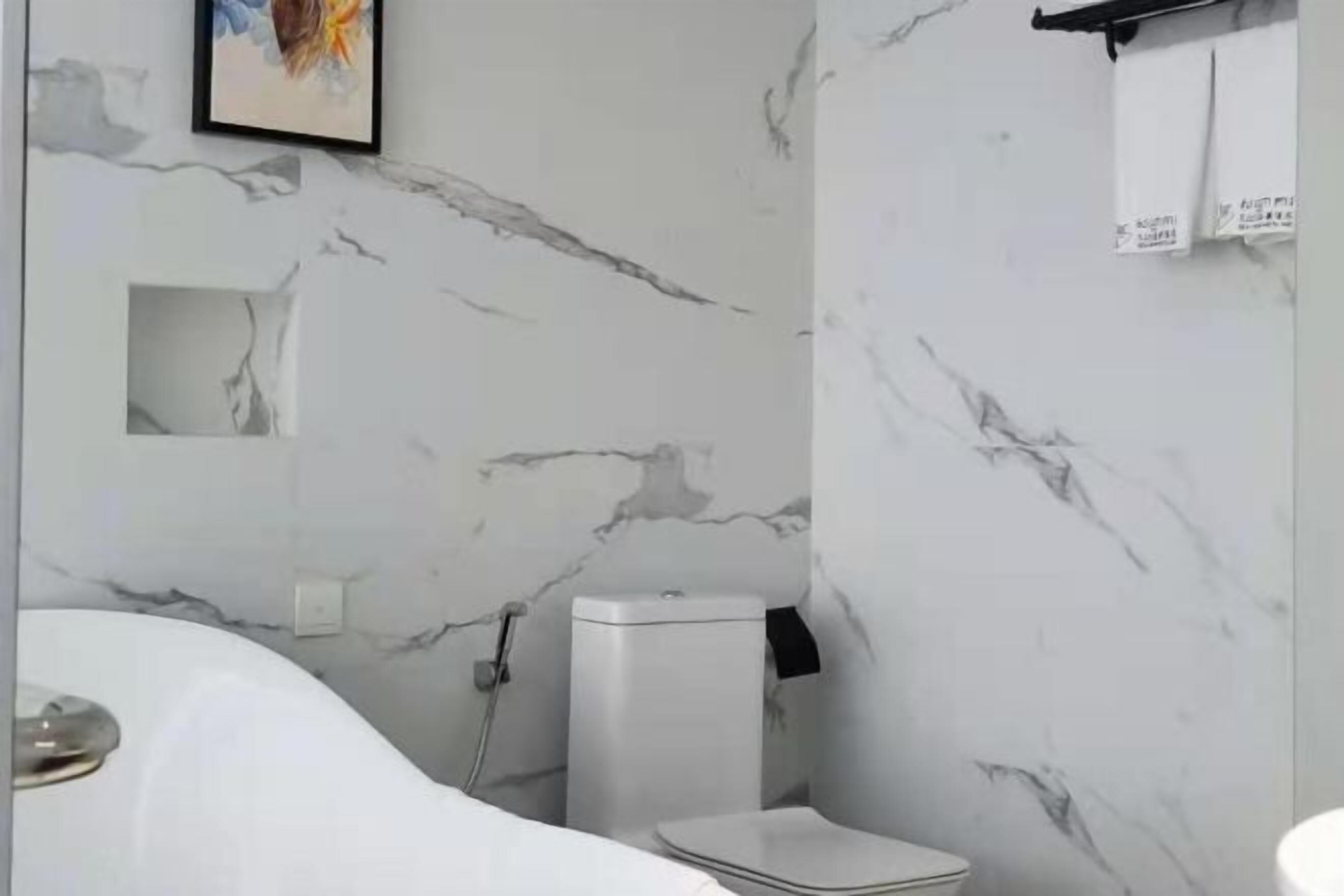 A bathroom with a marble wall, a toilet, and a bathtub.