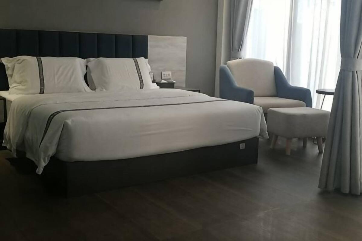 A hotel room with a large bed, a chair, a small table, and a nightstand.