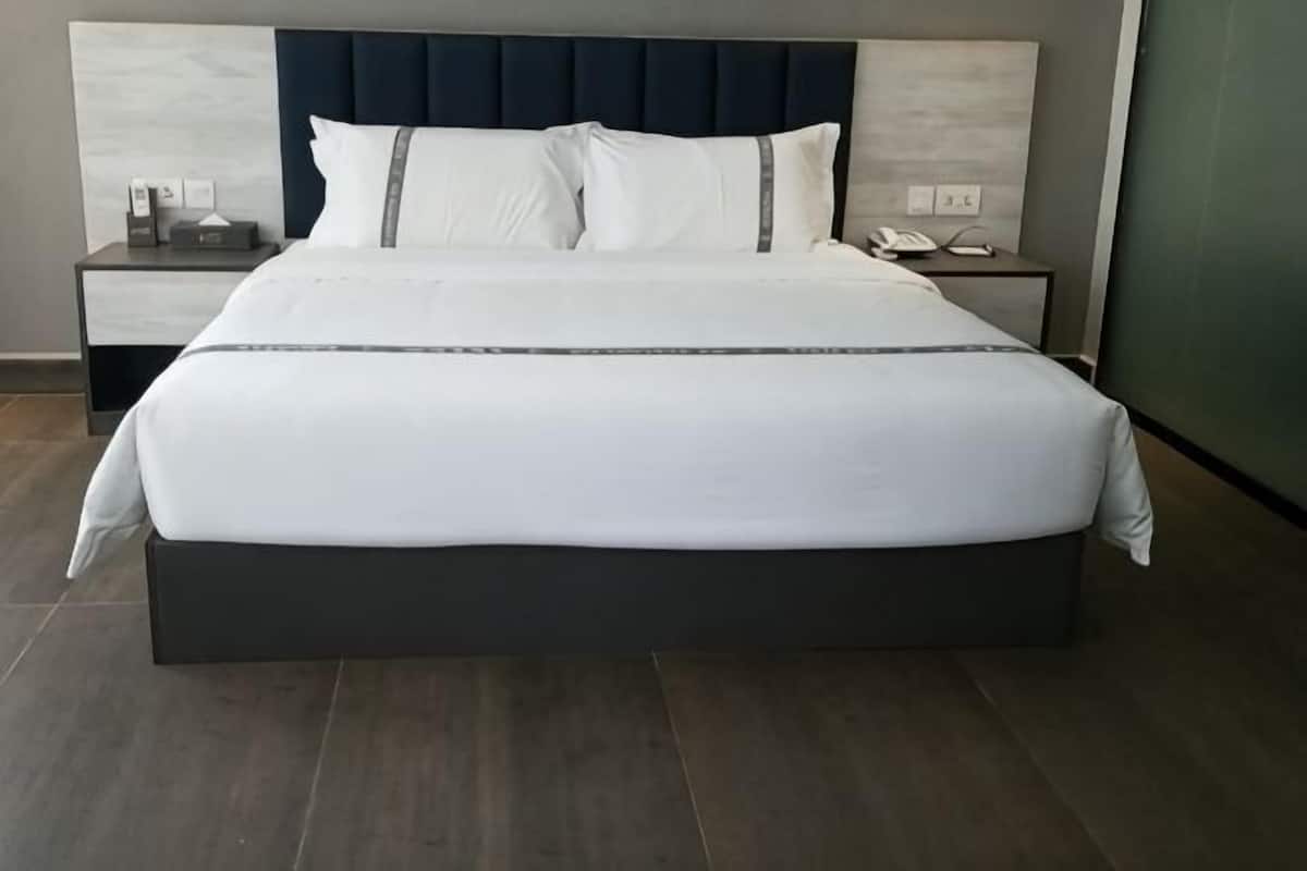 A large bed with a dark headboard, white bedding, and a bedside table with a lamp and phone.