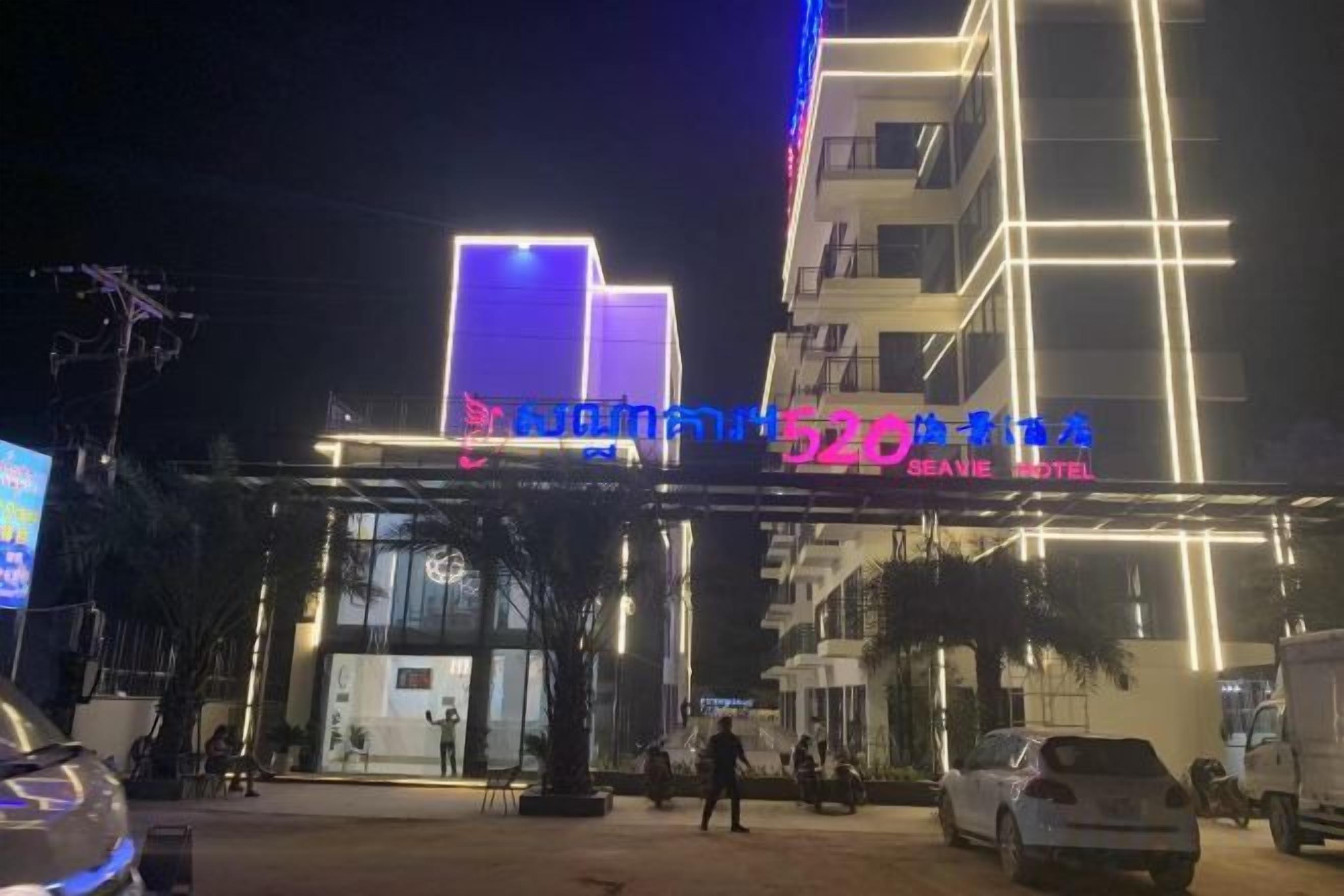 Entrada de un hotel con diseño moderno, destacando un letrero llamativo y un vestíbulo cubierto.