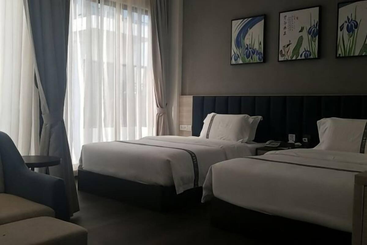 A hotel room with two beds, a chair, a nightstand, and artwork on the wall.