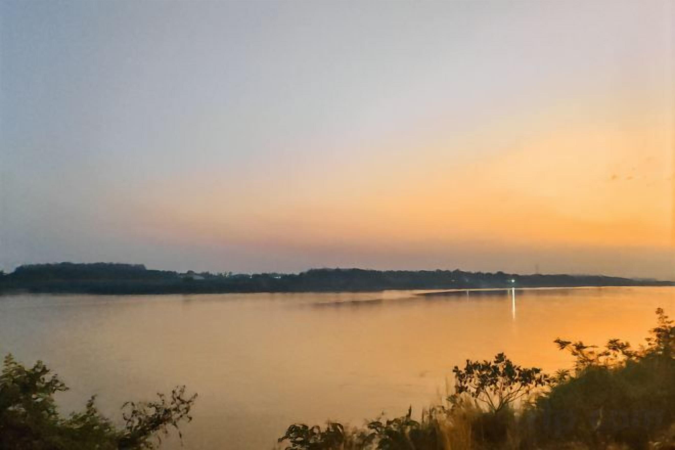 A calm body of water with a distant shoreline and a bridge.