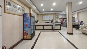 Un espace d’accueil d’hôtel comprenant un comptoir de réception, une grande enseigne encadrée et une affiche représentant des fruits.