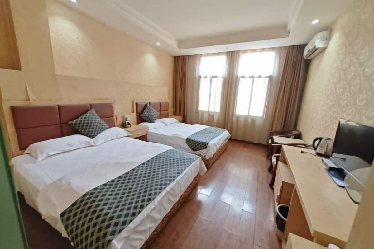 Una habitación de hotel con dos camas, un escritorio con televisor y una ventana con cortinas.