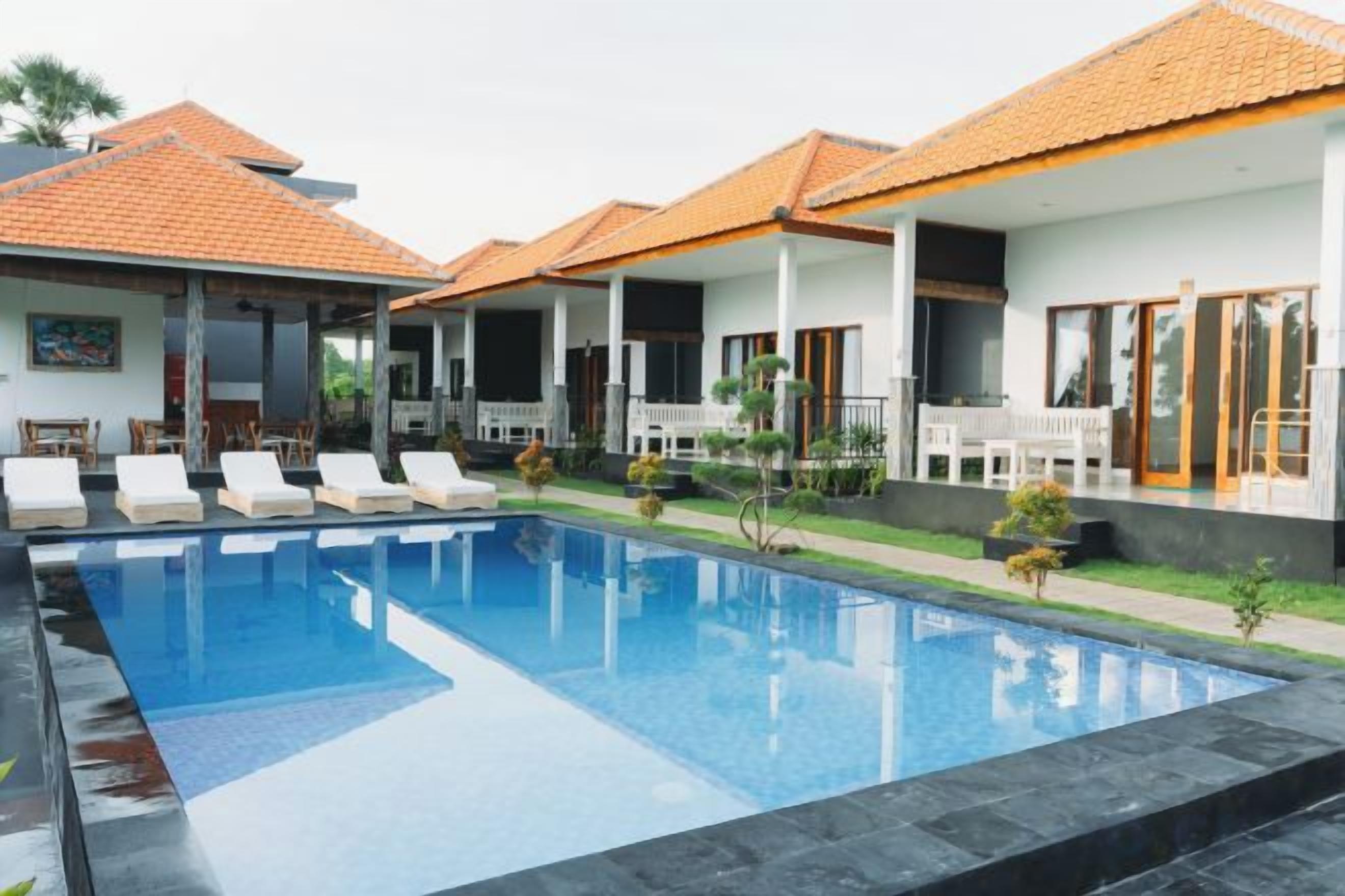 A swimming pool with lounge chairs, a covered patio area, and a house with a tiled roof.