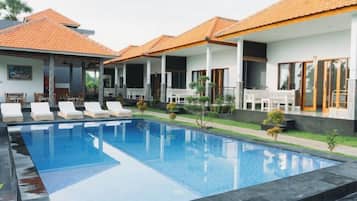 A swimming pool with lounge chairs, a covered patio area, and a house with a tiled roof.