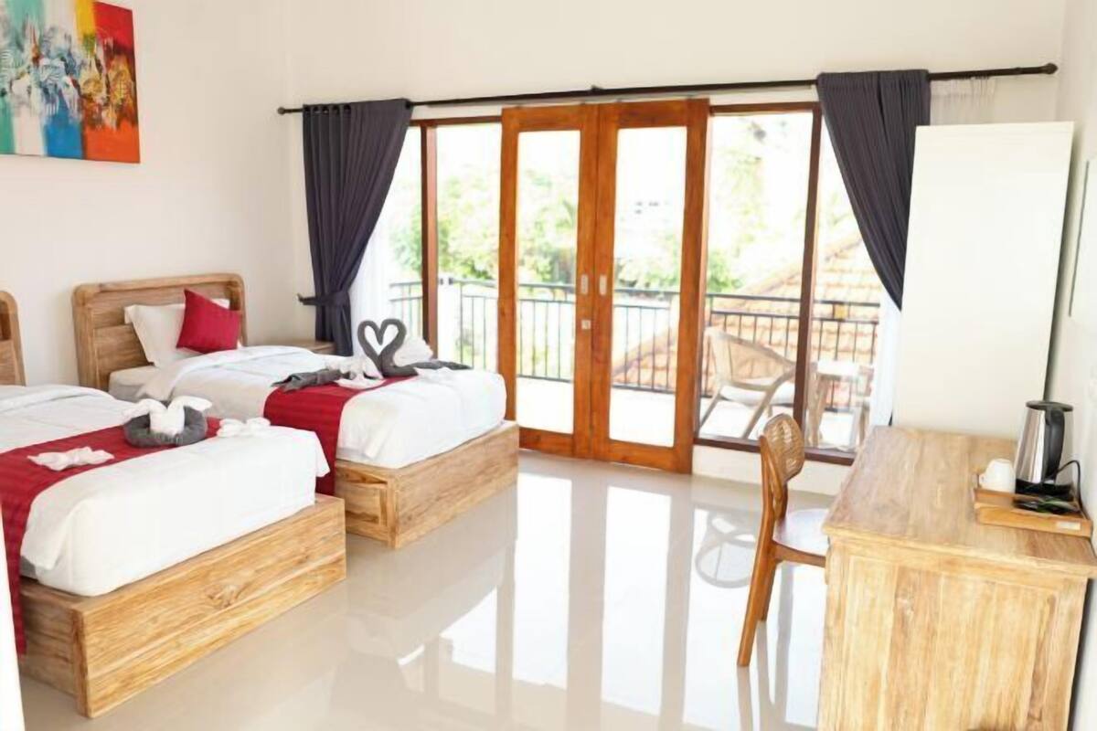 Une chambre d’hôtel avec deux lits en bois, un bureau, une chaise et un balcon doté d’une rambarde.