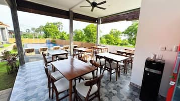 An outdoor patio with tables and chairs, a ceiling fan, and a pool in the background.
