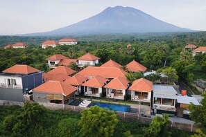 A resort with multiple buildings, a swimming pool, and a mountain in the background. - Oceanus Tulamben Dive Resort (Bali)