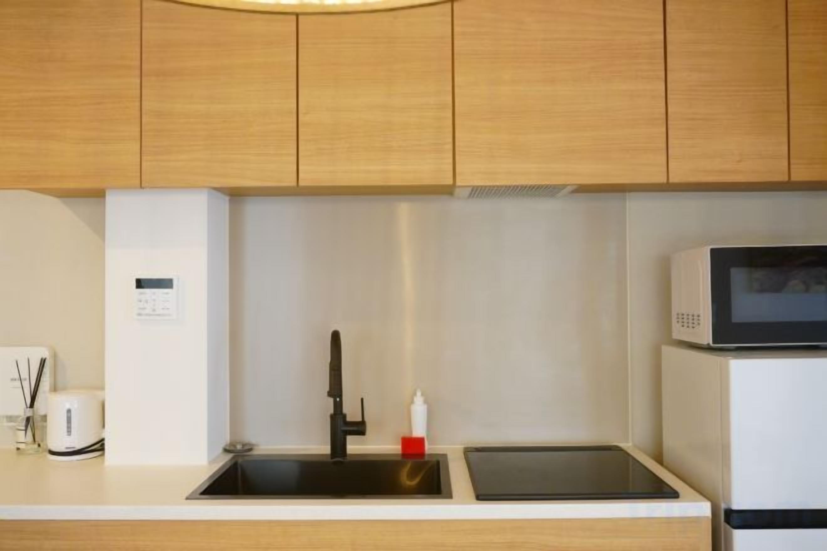 A kitchen with wooden cabinets, a sink, a microwave, and a digital display.