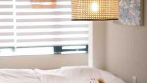 Une chambre à coucher avec un lit, une table de chevet ornée d’un vase de fleurs et une fenêtre avec des stores.