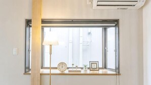 Une pièce avec une fenêtre, une lampe, une horloge et une petite table ornée d’objets décoratifs.