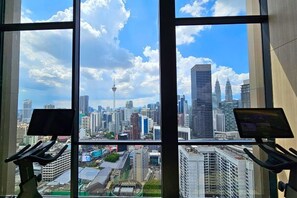 A room with a large window offering a view of a city skyline, exercise equipment, and a laptop on the windowsill. - Axon Bukit Bintang by Janice's Homestay (Kuala Lumpur)