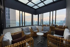 Een terras op het dak met rieten meubels, een klein rond tafeltje en uitzicht over de stad.
