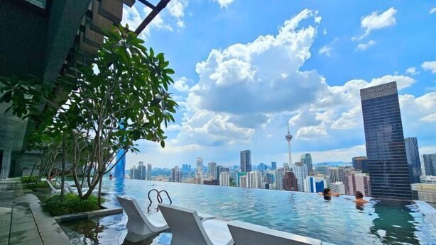 An infinity pool with city views, lounge chairs, and a modern building in the background. - Axon Bukit Bintang by Janice's Homestay (Kuala Lumpur)