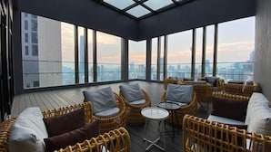A high-rise balcony with wicker furniture and a glass ceiling, overlooking a cityscape. - Axon Bukit Bintang by Janice's Homestay (Kuala Lumpur)