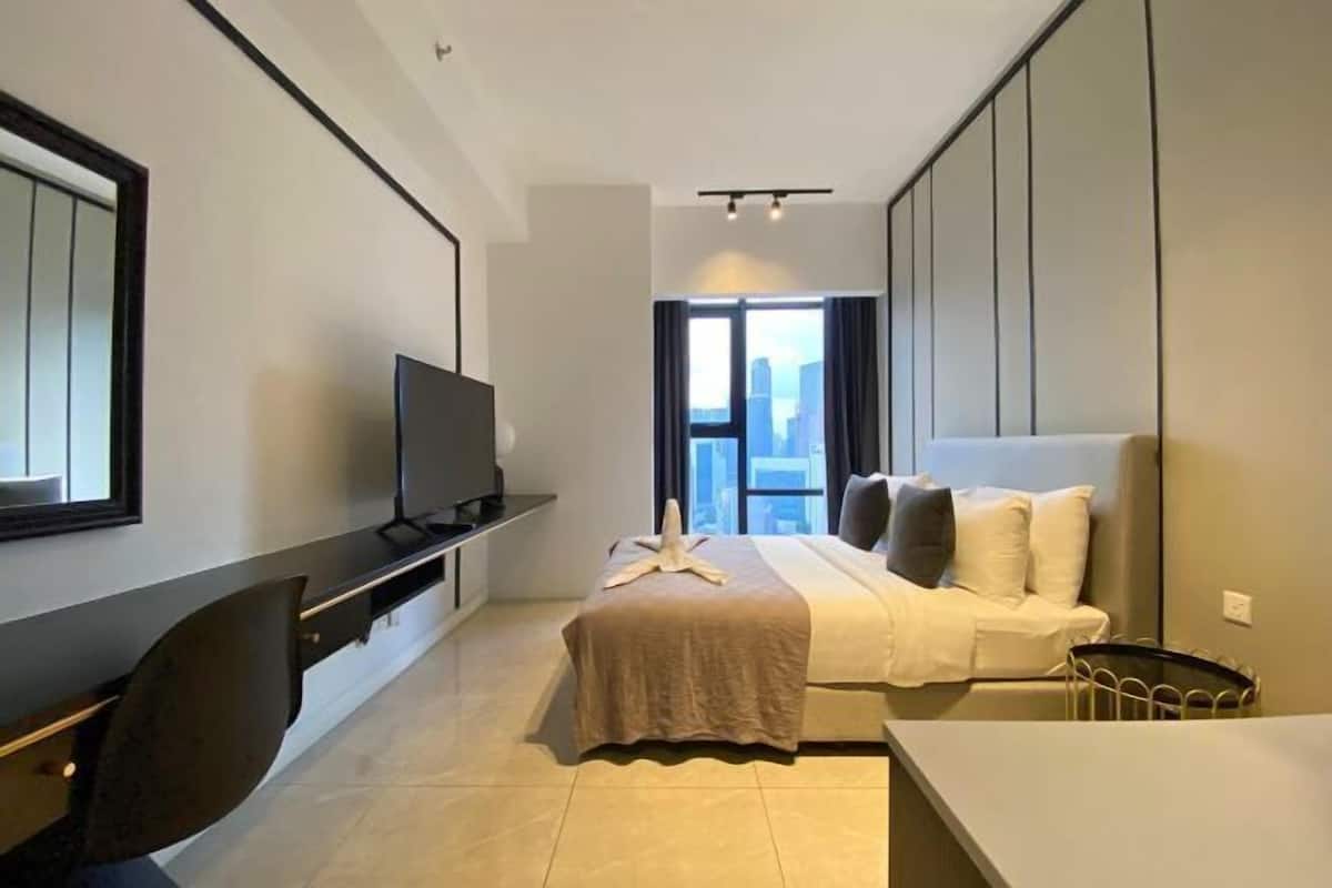 Habitación de hotel moderna con cama, escritorio, televisor y un amplio ventanal con vistas a la ciudad.