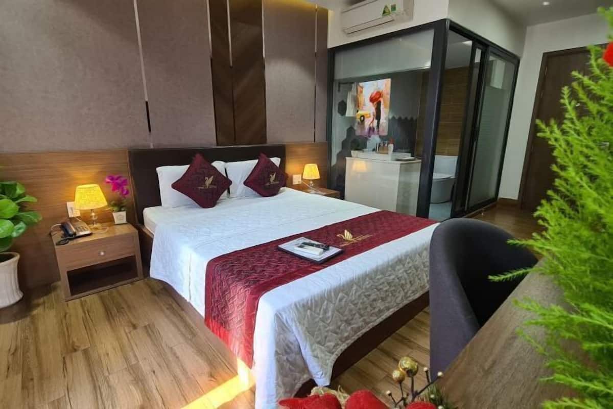 A hotel room with a bed, bedside tables, a nightstand, a desk, a chair, and a potted plant.