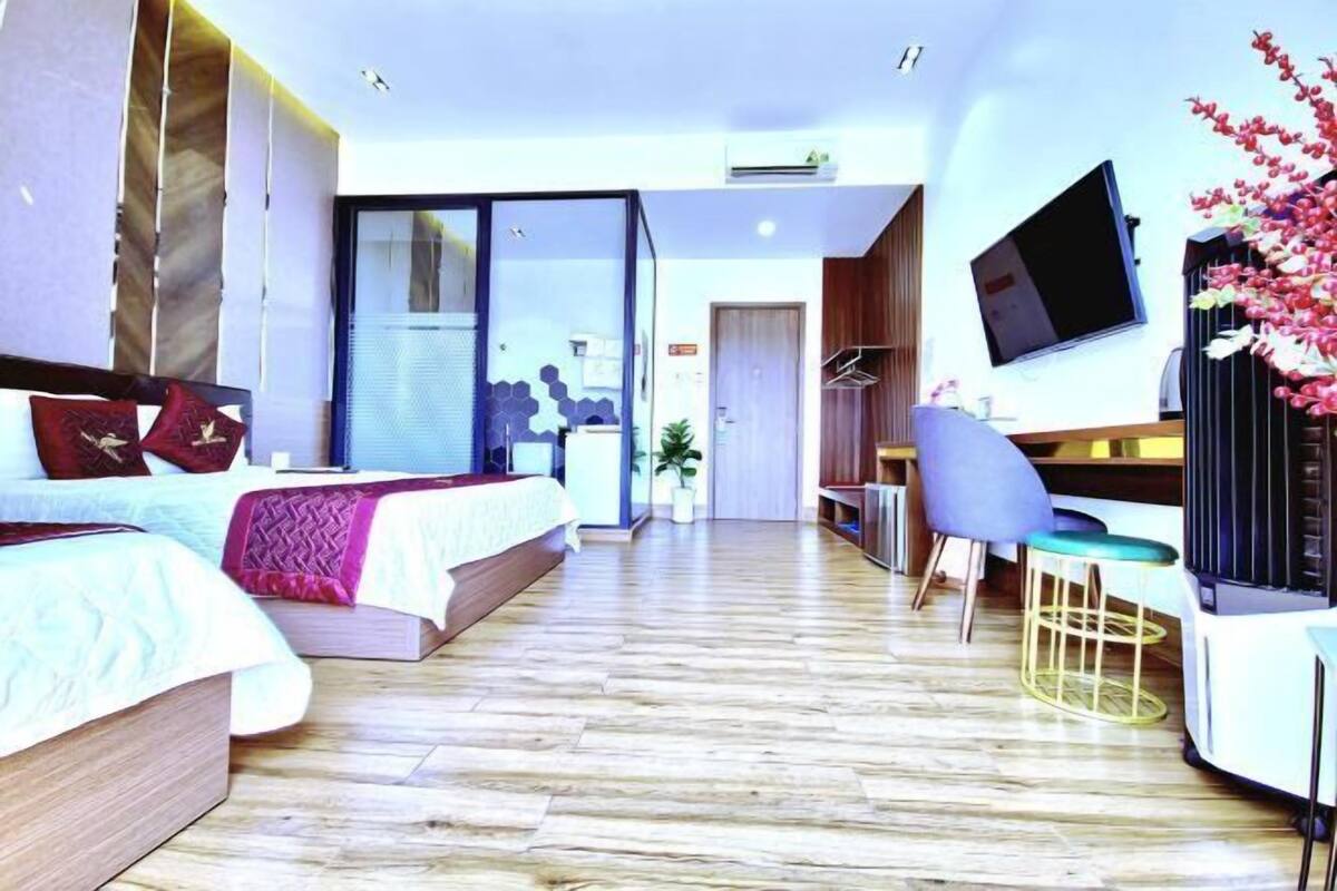A modern hotel room with a large bed, a desk, a chair, a TV, and a large window.