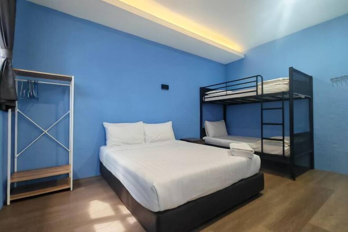 Una stanza con un letto singolo, un letto a castello, una panca di legno e un appendiabiti.