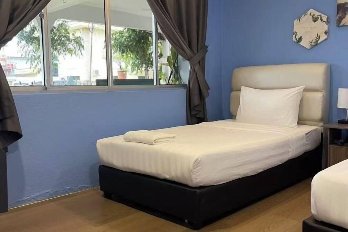 Un letto singolo con materasso e cuscini bianchi, una testiera scura e una finestra con tende.